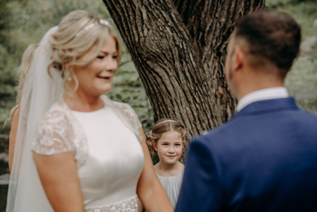 Bridesmaid looking up at mum and dad during ceremony under Gapstow Bridge