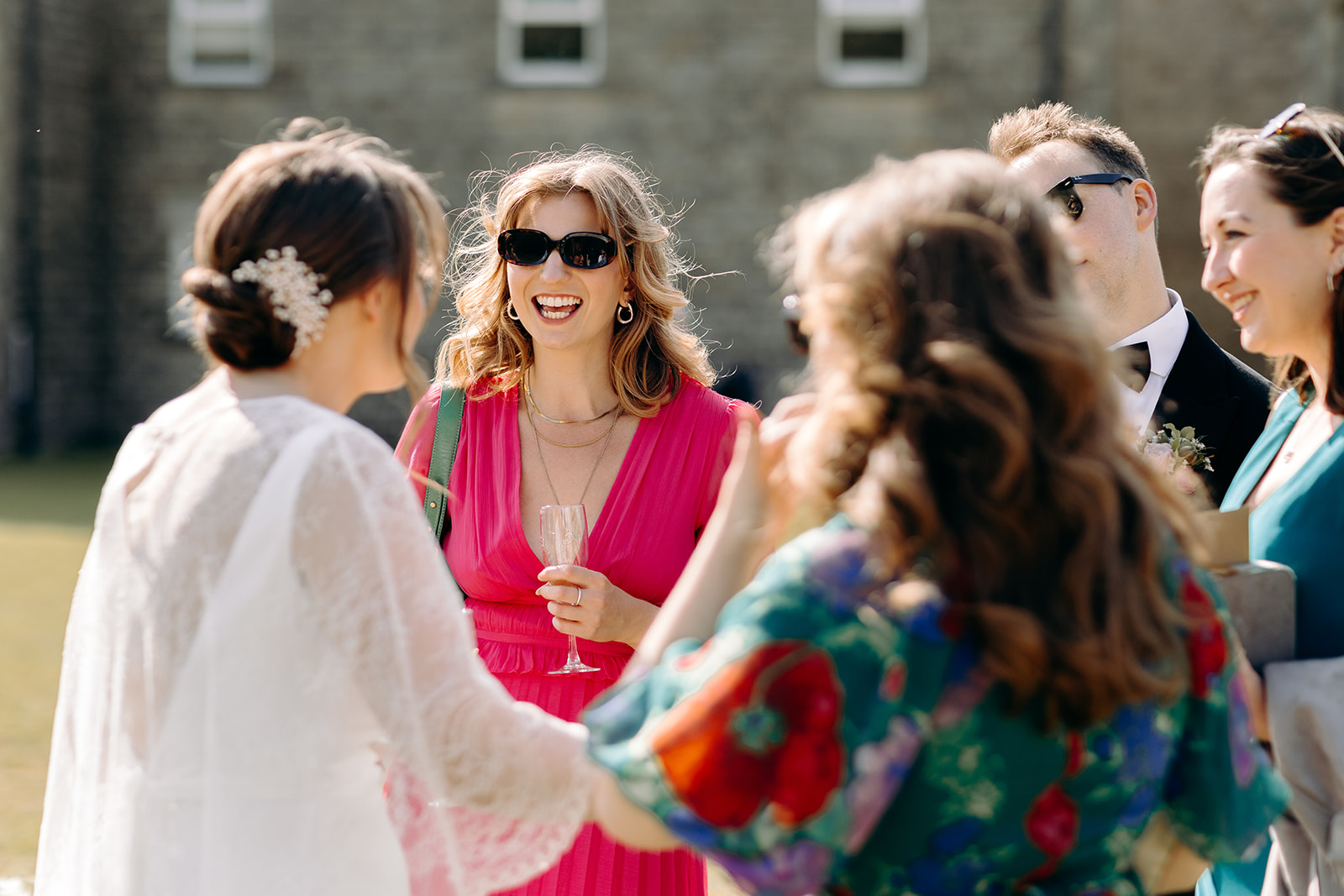 Bride laughing with group of three female guests, colourful outfits in bright sunlight.