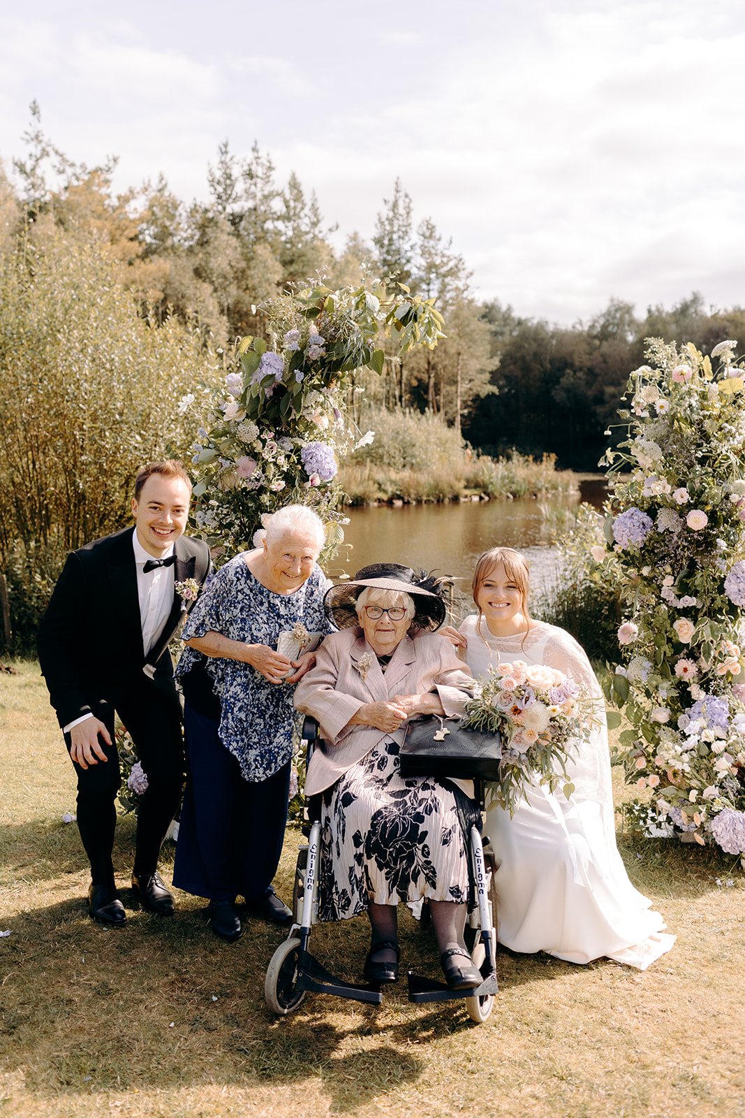 Couple posing with an older couple beside the floral arch, multigenerational wedding photo.