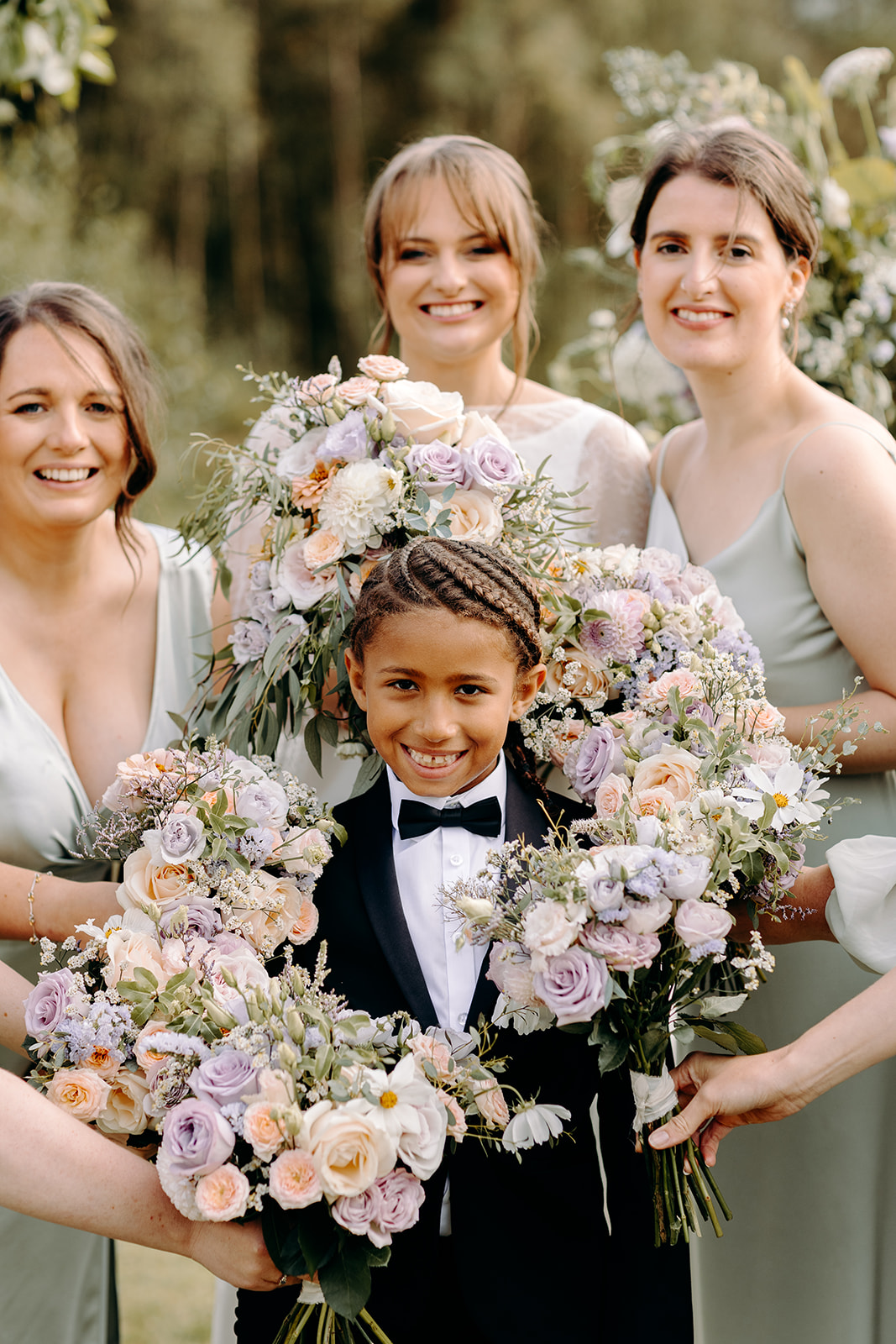 Page boy posing with bridesmaids flowers in golden sunlight, joyful and fun wedding photography in Derbyshire.
