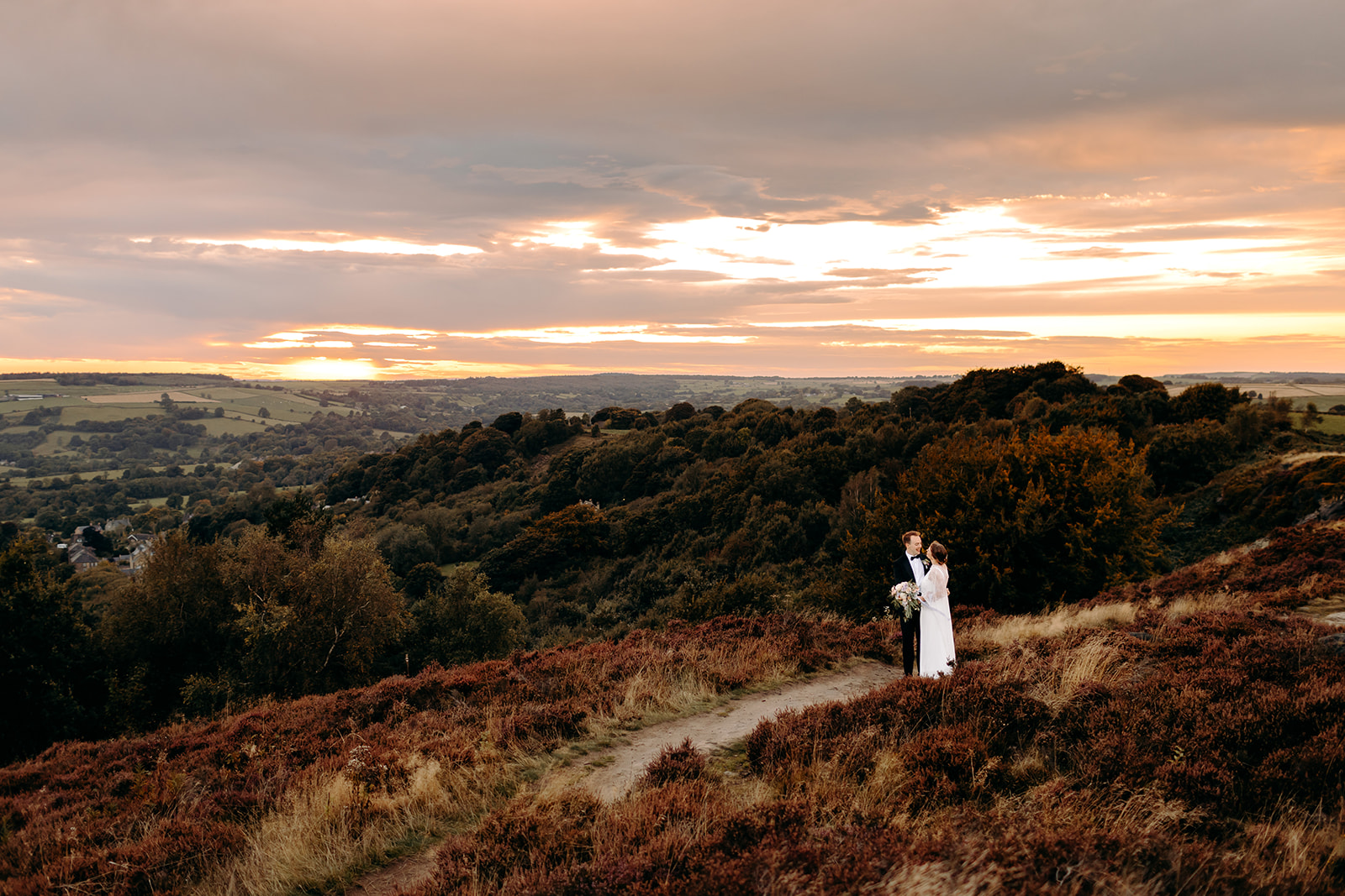 The newlyweds walk through a heather-lined trail at sunset – romantic Darwin Lakes Holiday Village wedding portrait.
