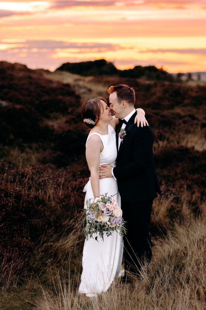 Groom wraps arms around bride as golden light hits the horizon – dreamy Peak District wedding moment.