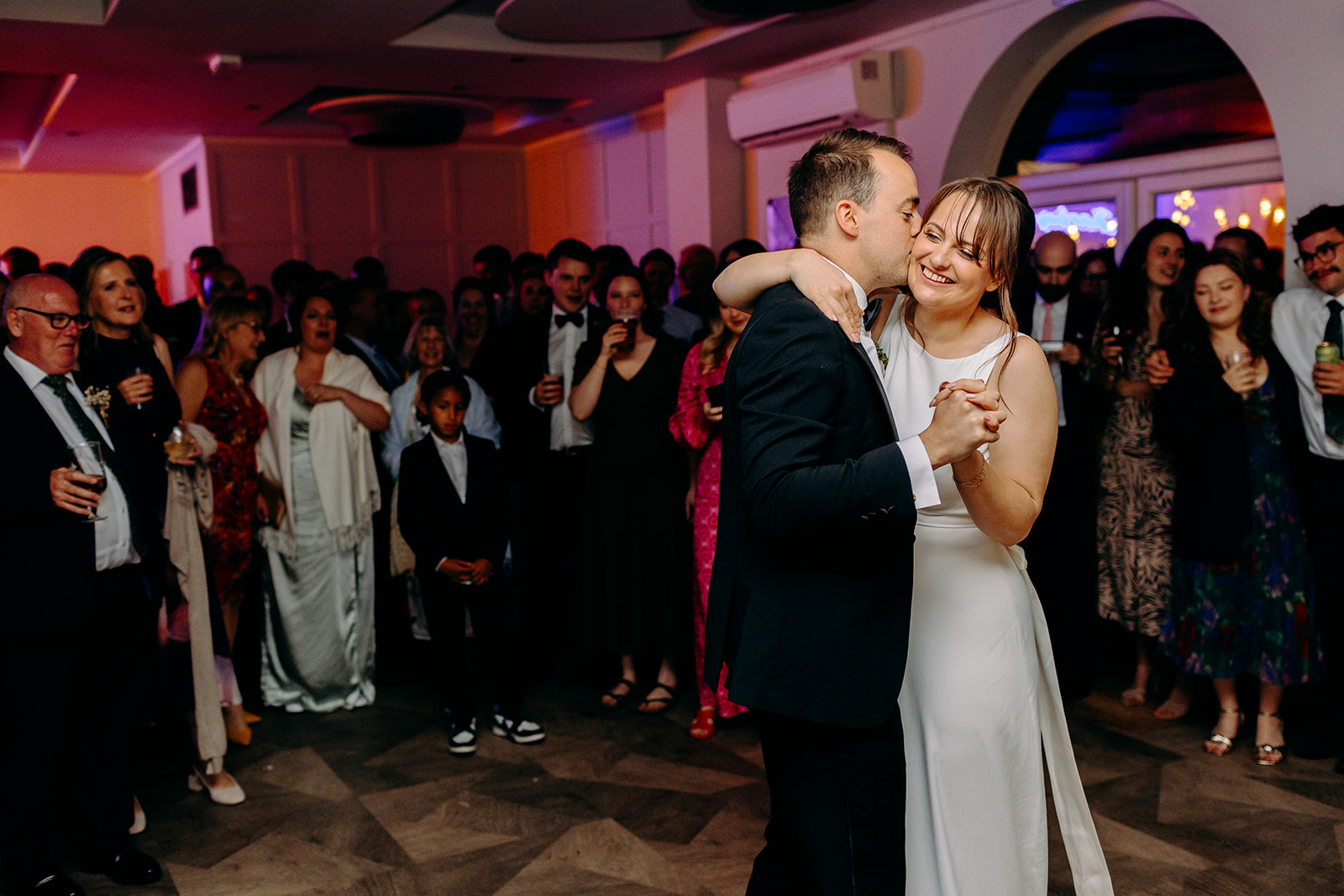The couple dancing with joyful guests surrounding them — natural wedding photography moment.