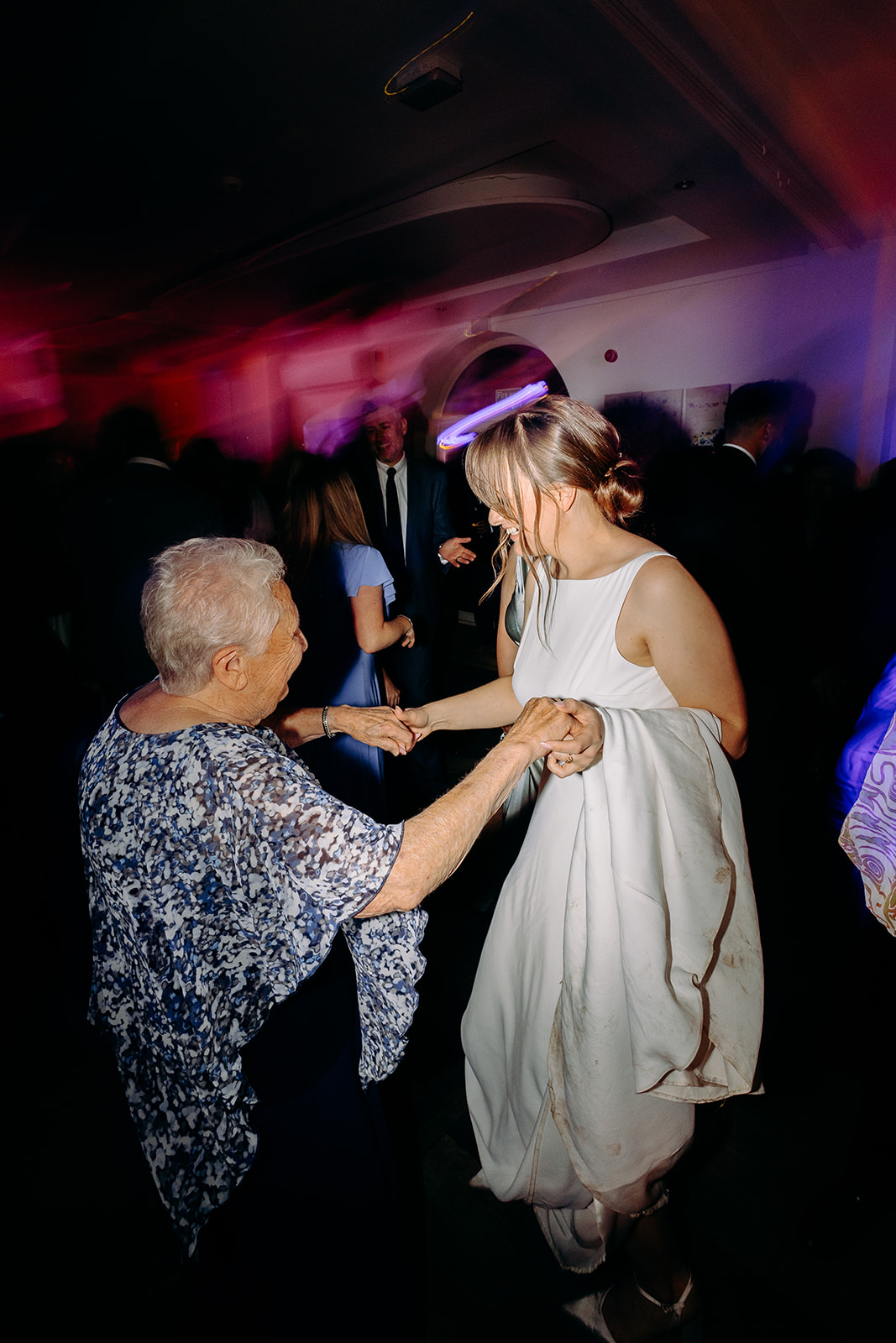 Natural wedding photography of the bride dancing joyfully with her grandma under pink and purple disco lights.