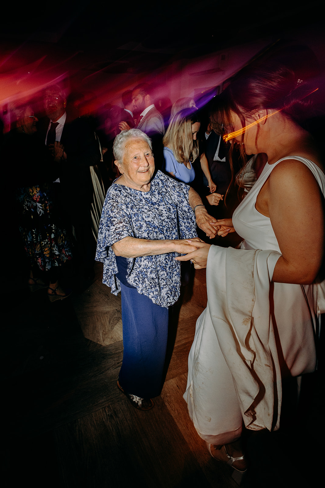 Natural wedding photography of the bride dancing joyfully with her grandma under pink and purple disco lights.