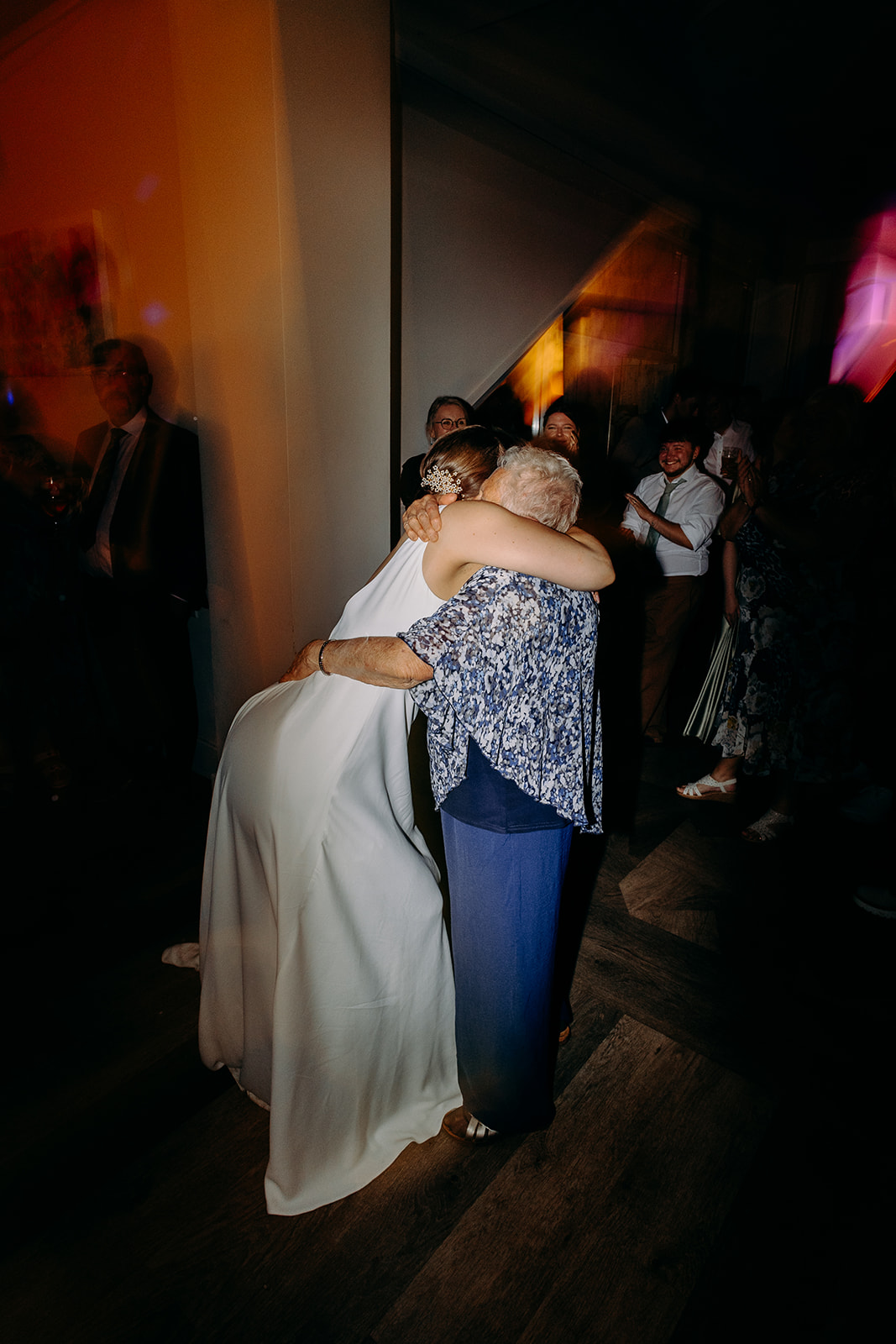 Natural wedding photography of the bride dancing joyfully with her grandma under pink and purple disco lights.