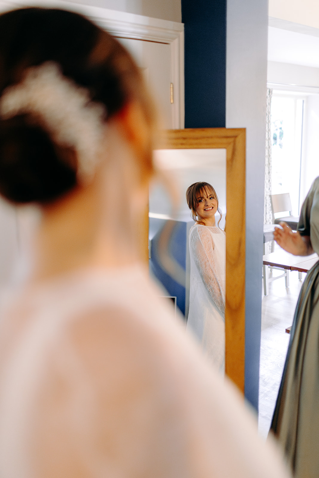 Soft mirror portrait of bride seeing her wedding dress on, showing natural light and detail.