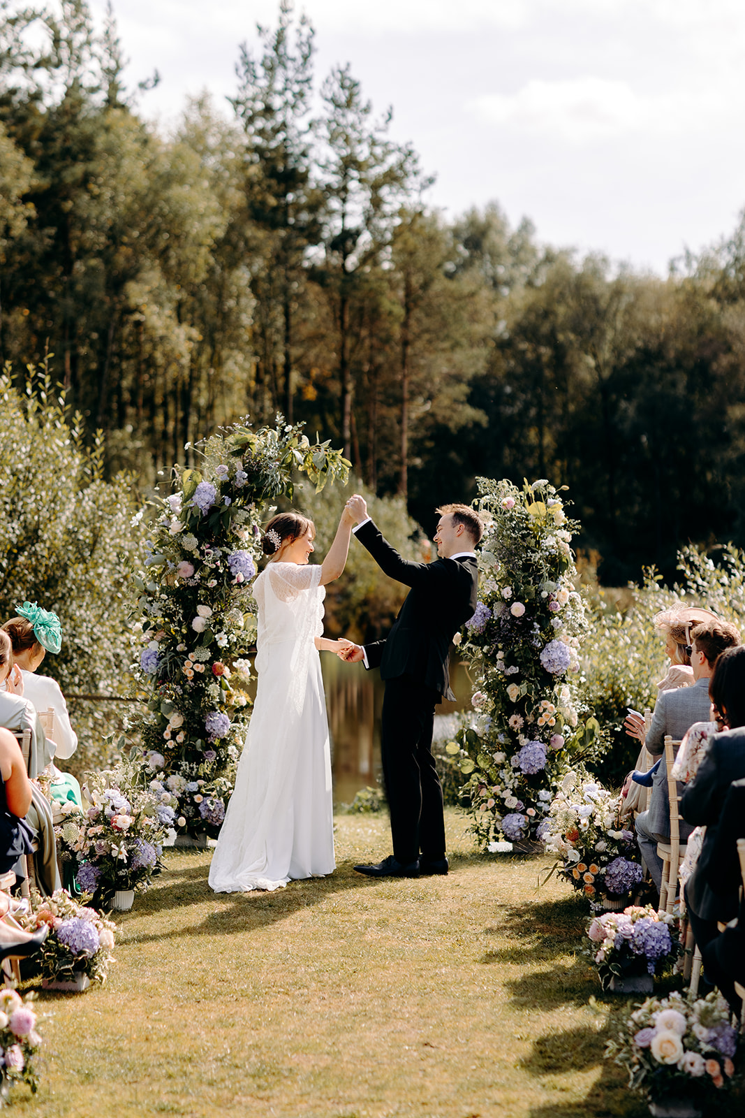 Natural photo of the bride and groom cheering after their first kiss, with wild flowers and Darwin Lake behind them - natural, candid wedding photography in the Peak District.