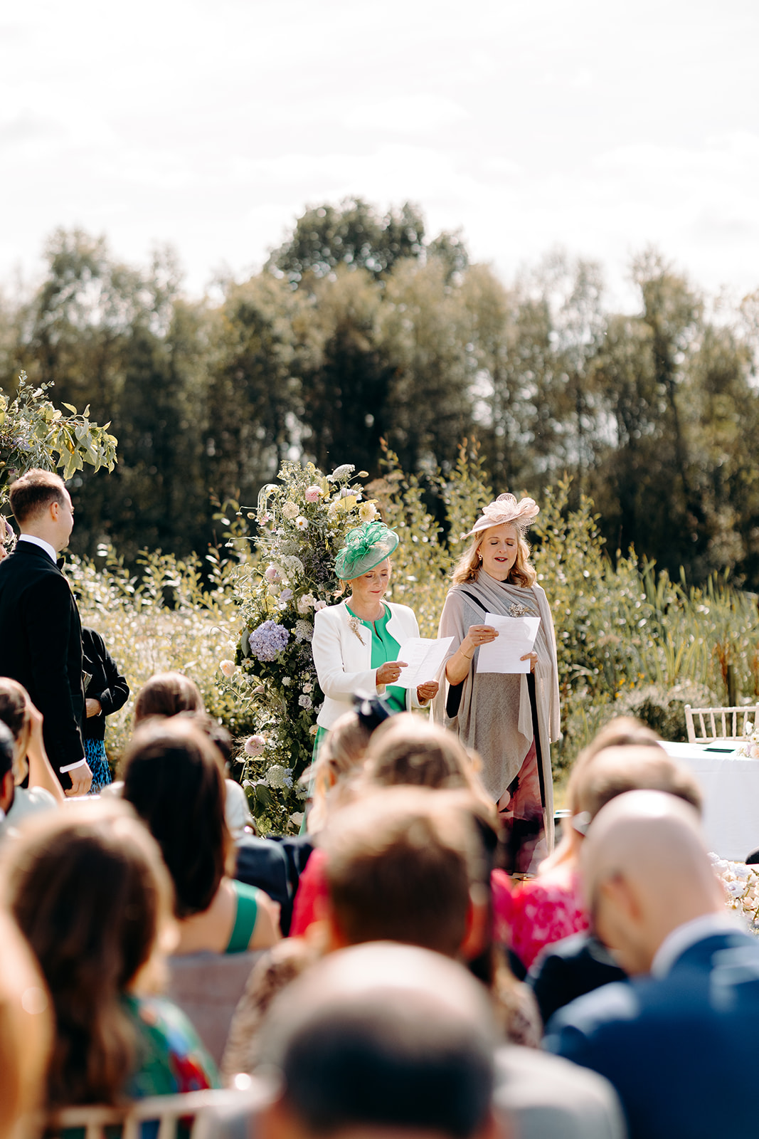 Natural photo from the guest's perspective of the two mum's making a reading during outdoor, summer wedding ceremony in the Peak District.