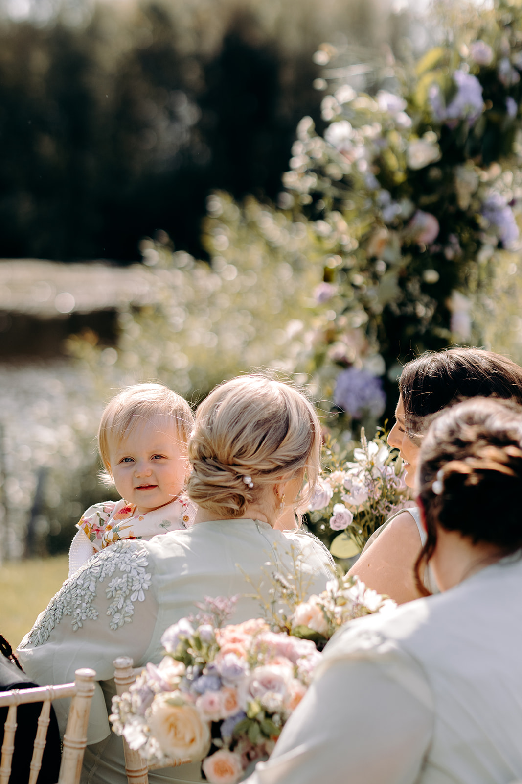 Photo of cheeky flower girl peering through the guests and looking at the camera - candid wedding photography in Derbyshire.