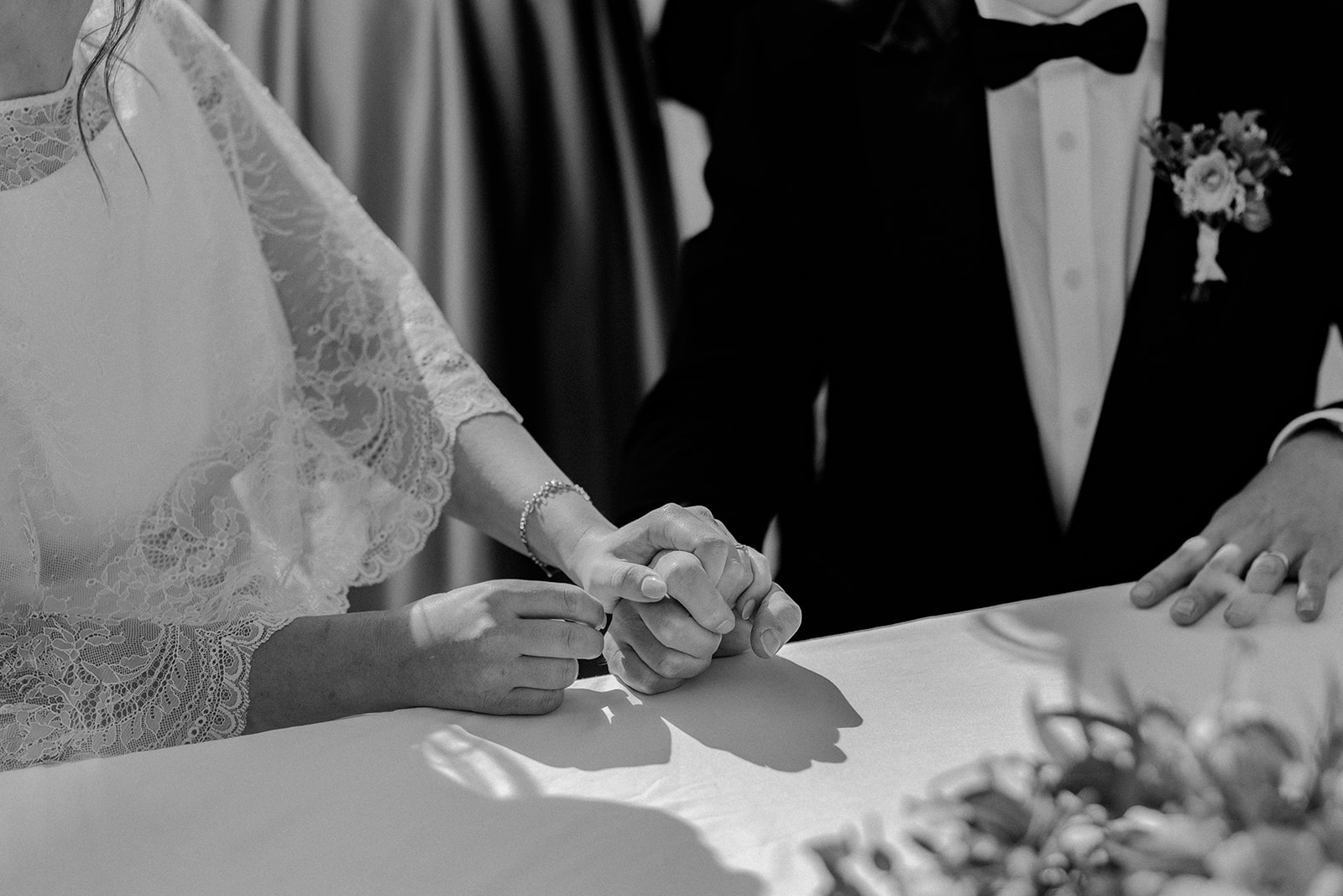 Black and white detail photo of bride and groom holding hands whilst signing the register, natural, documentary style wedding photography in the Peak District.