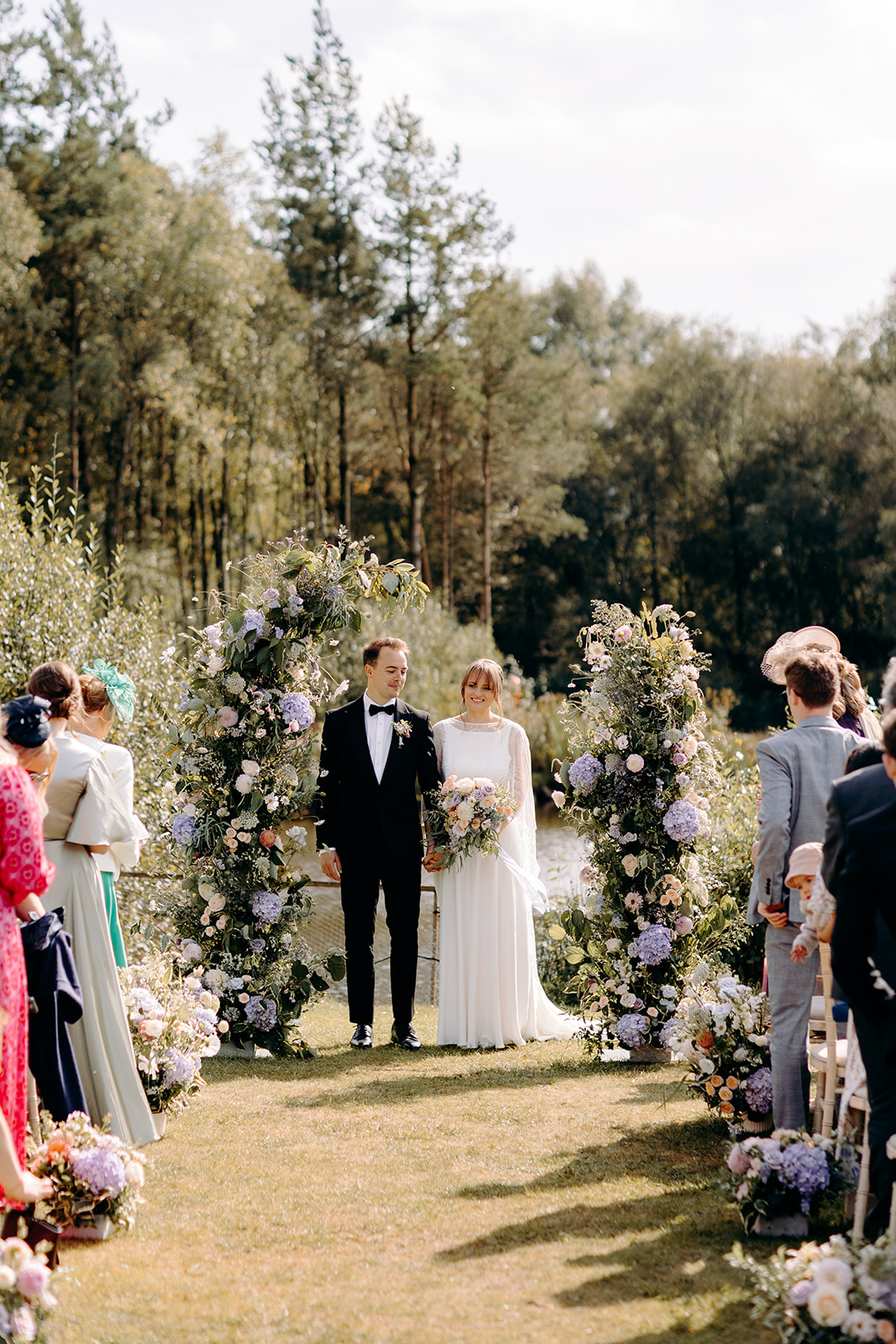 Bride and groom posing by floral ceremony arch, rustic Peak District backdrop.