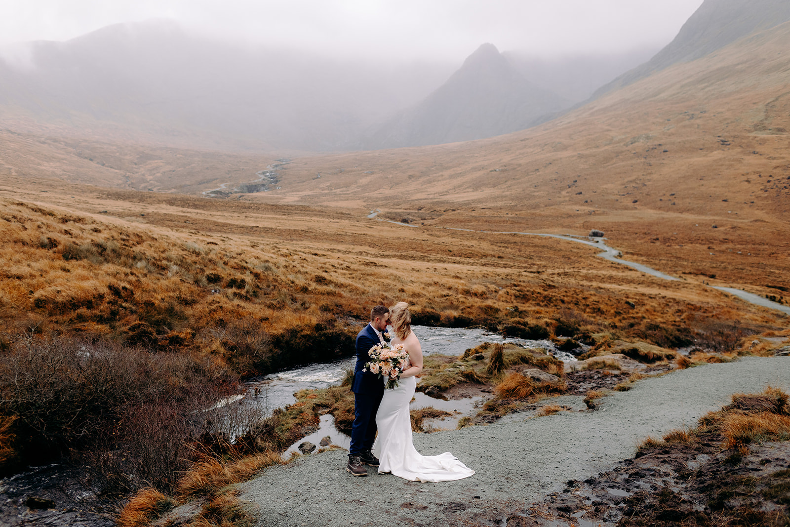 Couple walking hand in hand on a winding path through the rugged landscape of the Isle of Skye – eloping in Scotland at its finest.