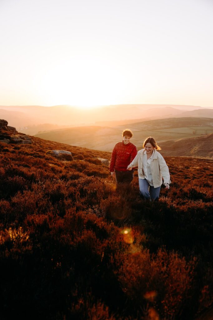 Couple walking through the heather on their pre-wedding photoshoot during the golden hour in the Peak District