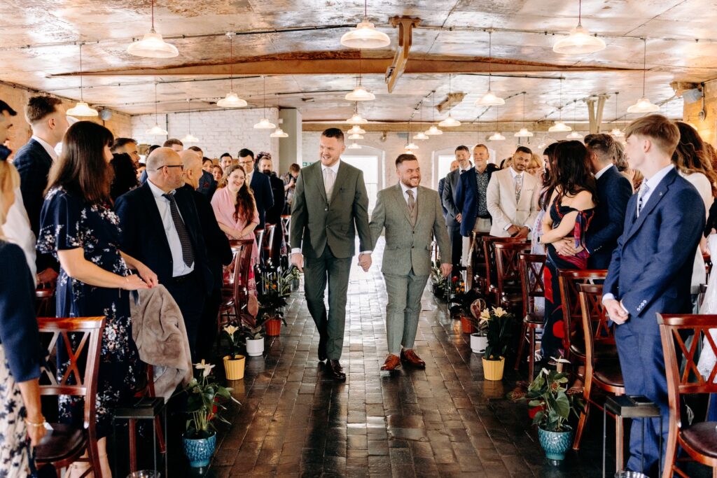 Two grooms walking down the aisle together to the ceremony at The West Mill