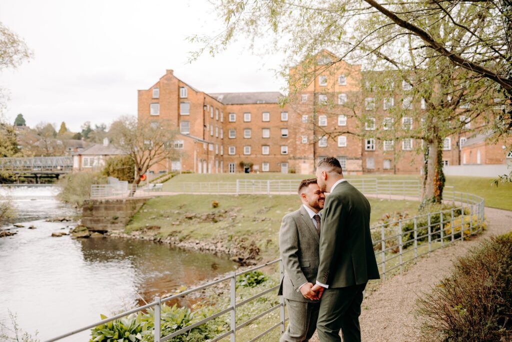Two grooms having their natural wedding portraits with The West Mill in the background