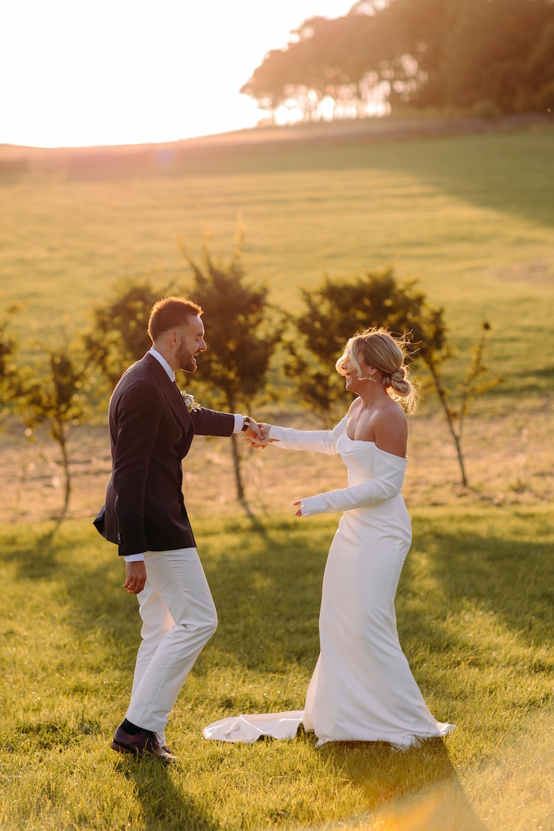 Fun, candid photo of the couple dancing barefoot on the grass at sunset, full of movement and laughter at their Bleaklow Farm wedding.
