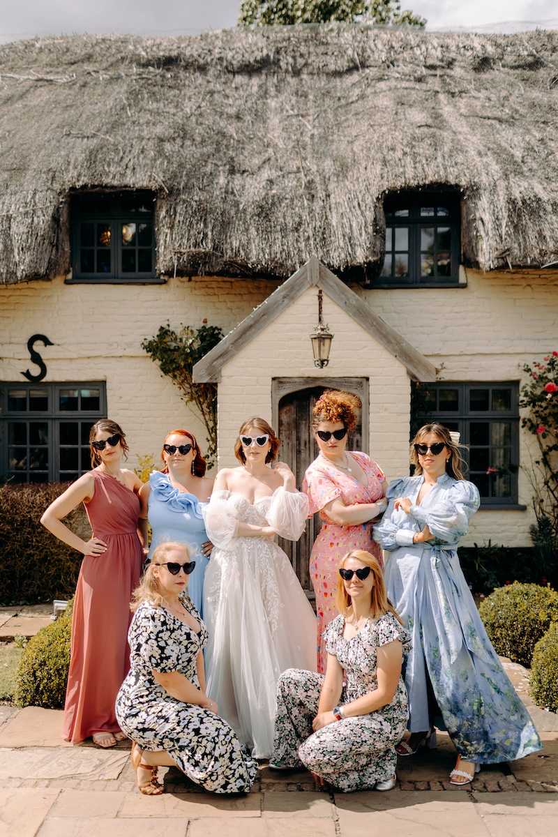 Relaxed group portrait of the bride and her friends outside the thatched main house at Marleybrook House wedding venue in Kent.