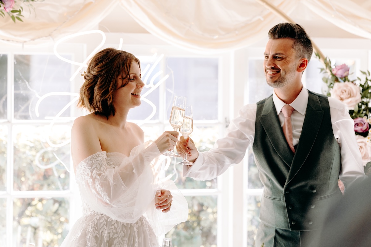 Bride and groom doing a cheers with prosecco during the speeches at a summer wedding at Marleybrook House