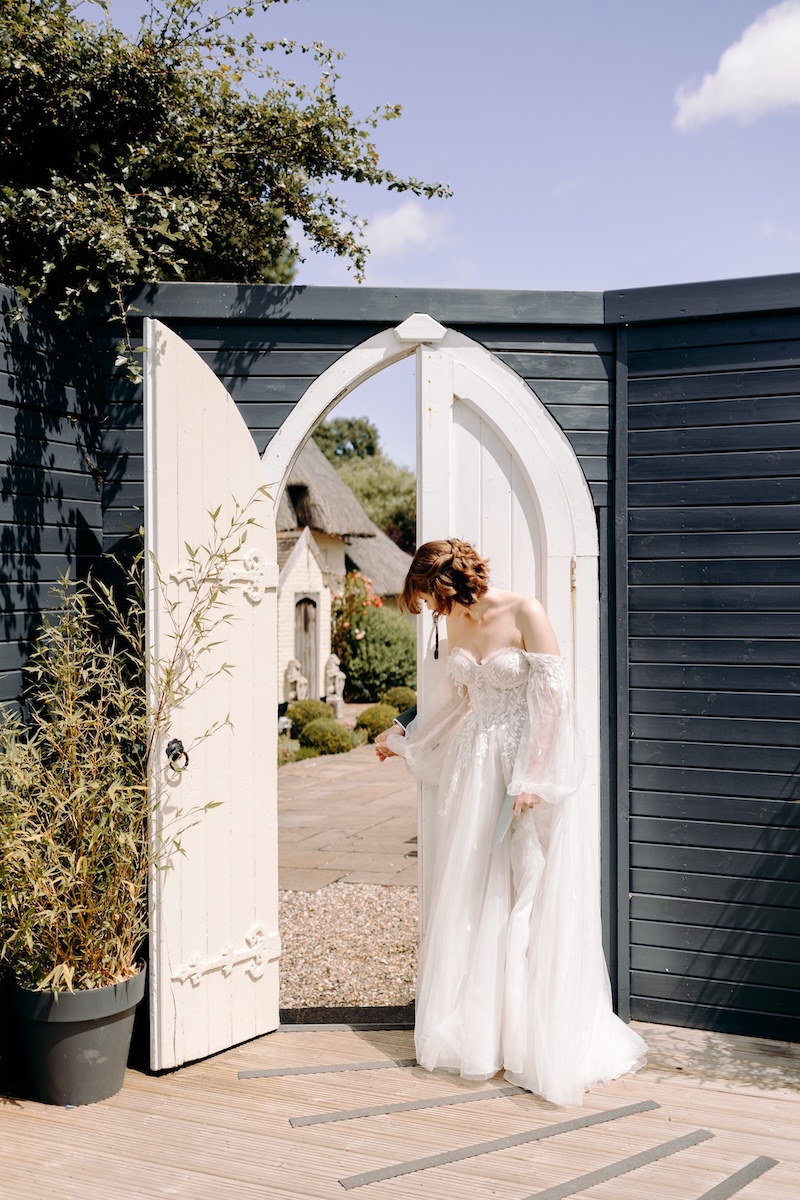 Bride exchanging letter with groom through white arched gate – romantic bridal portrait at Marleybrook House wedding venue.