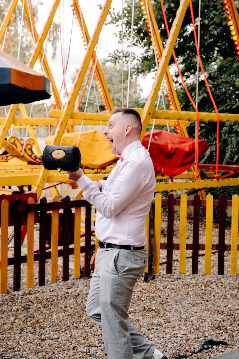 Guest laughs and holds a mallet at a fairground game, captured with a documentary photography style.