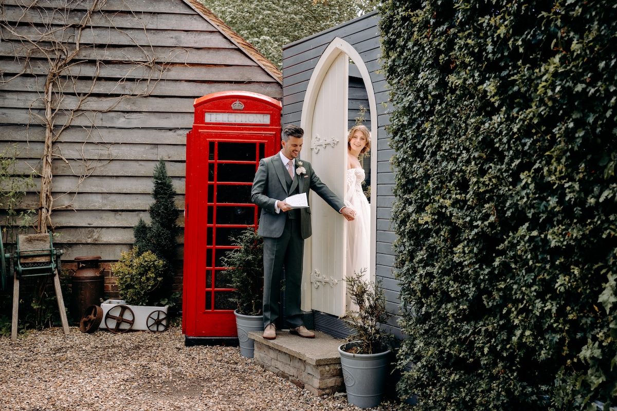Groom peeking out from behind a door near a red phone box – candid moment before ceremony at Marleybrook House.