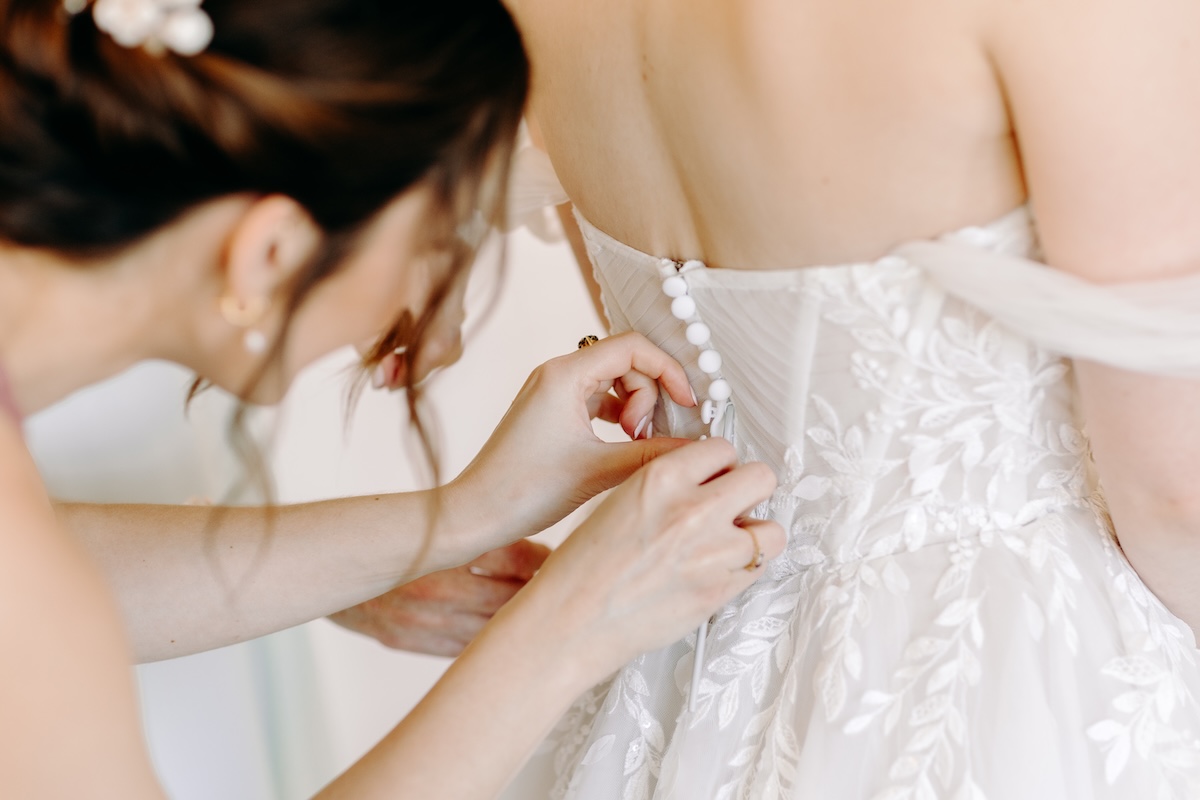 Close-up of hands tying the wedding dress – authentic, behind-the-scenes detail captured naturally.