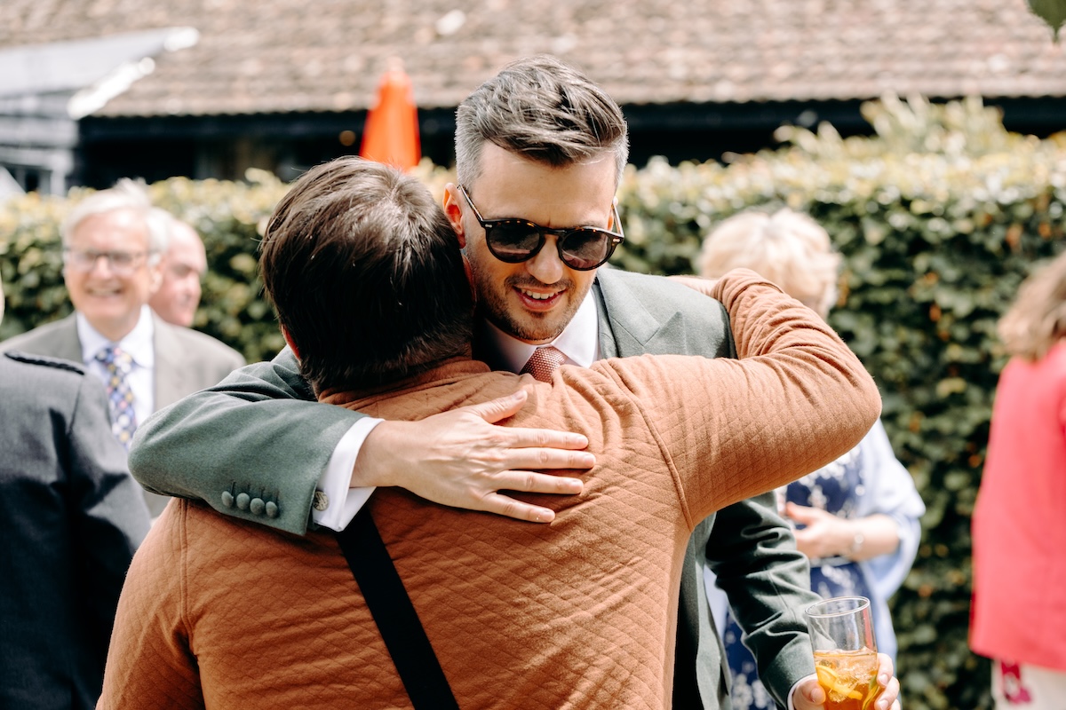 groom embracing a guest outdoors – candid, emotional arrival scene before the wedding ceremony.