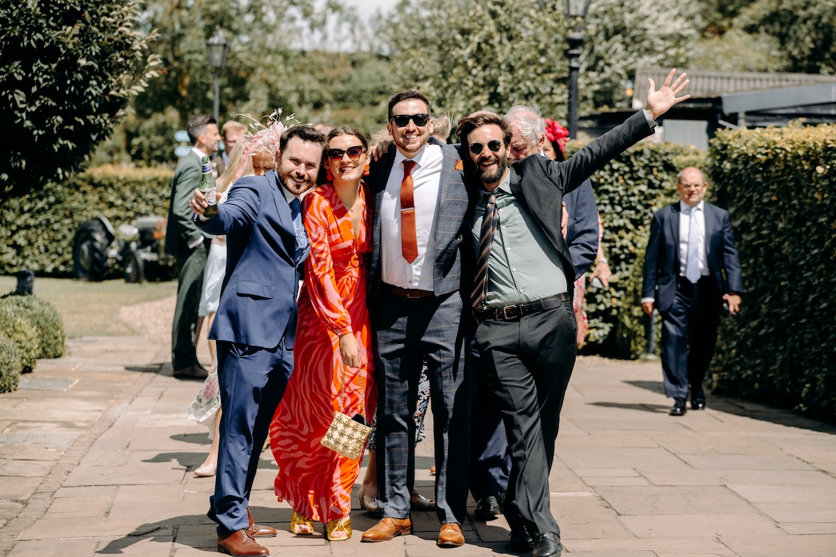 Bride and groom standing with a group of friends in vibrant outfits – fun wedding photography in Kent.