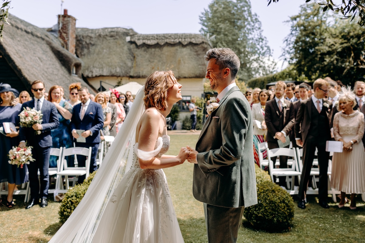 The bride beams at the groom mid-vows, her dress catching the sunlight – candid and joyful moment at a Kent garden ceremony.