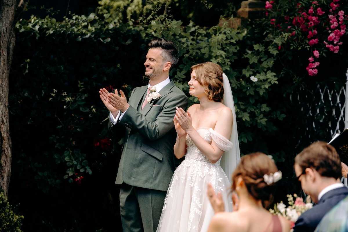 Groom laughs mid-vow, glancing at guests, with a joyful and relaxed energy – a fun moment during their outdoor Kent ceremony.