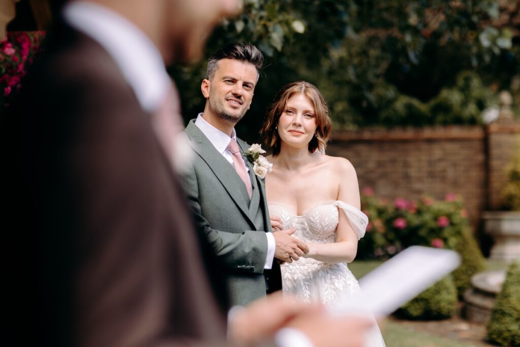 Over-the-shoulder shot of a guest doing a reading whilst the bride & groom listen – intimate storytelling at a Marleybrook House wedding.
