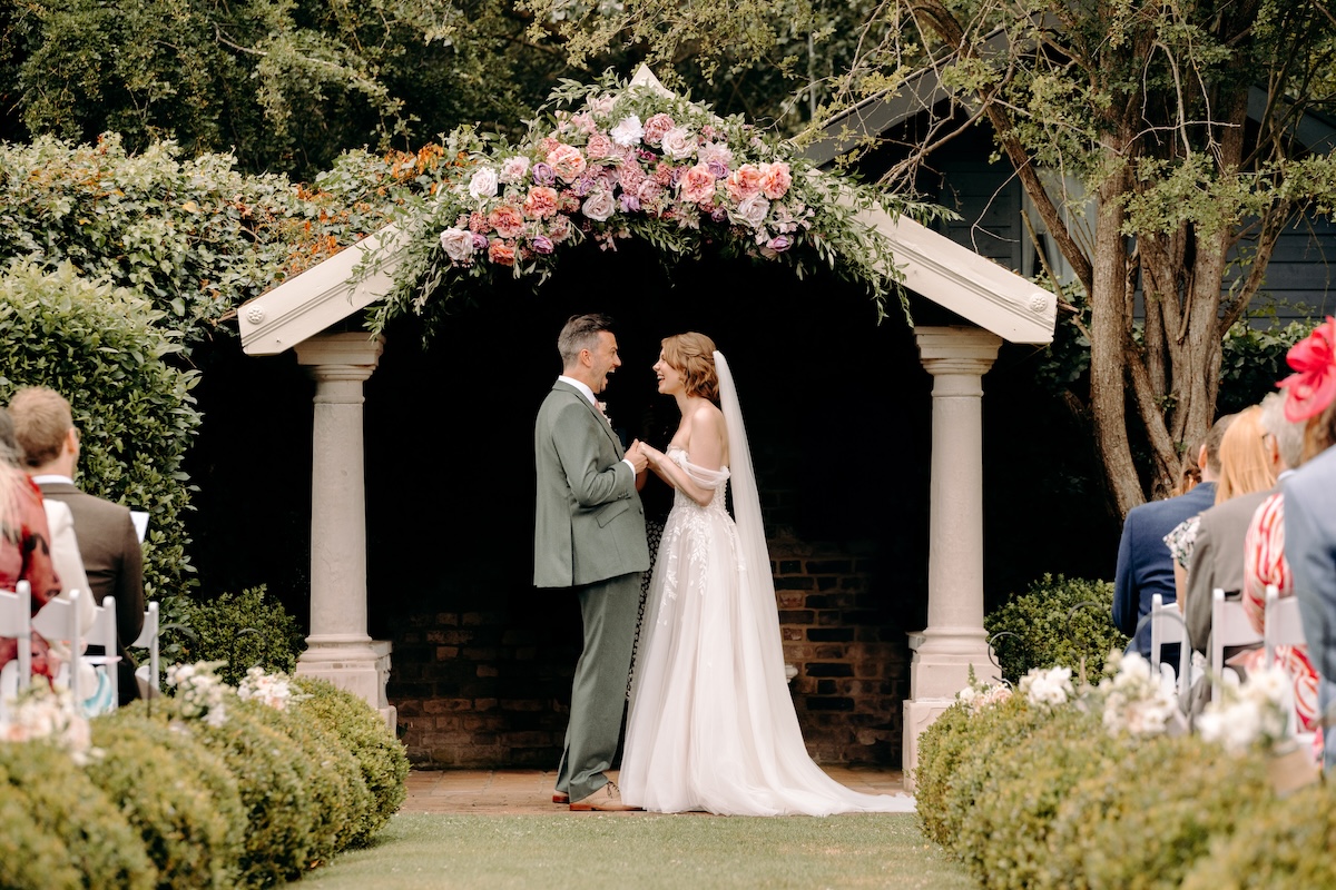 Bride and groom grinning at each other with the pavilion in the background – joyful ceremony at Marleybrook House.