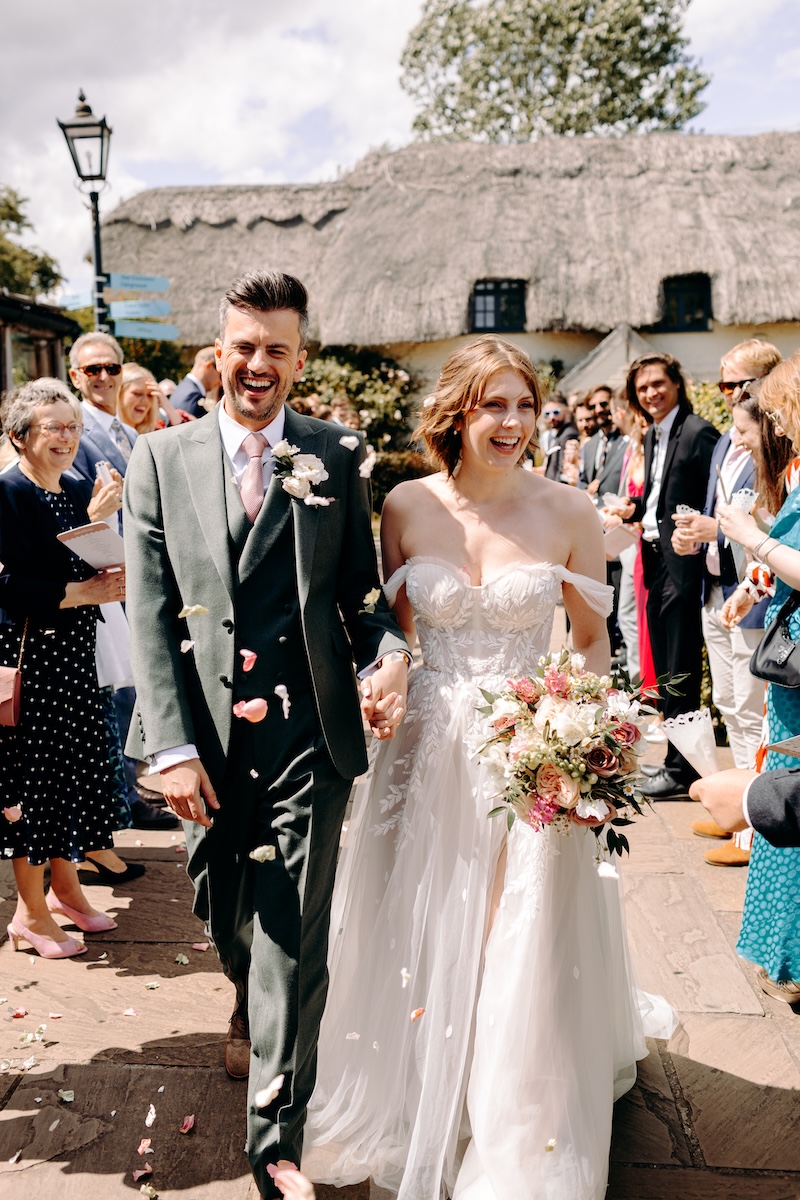 The couple pauses during the confetti walk, gazing lovingly at each other while holding hands; a soft, natural wedding photography moment full of connection at Marleybrook House.