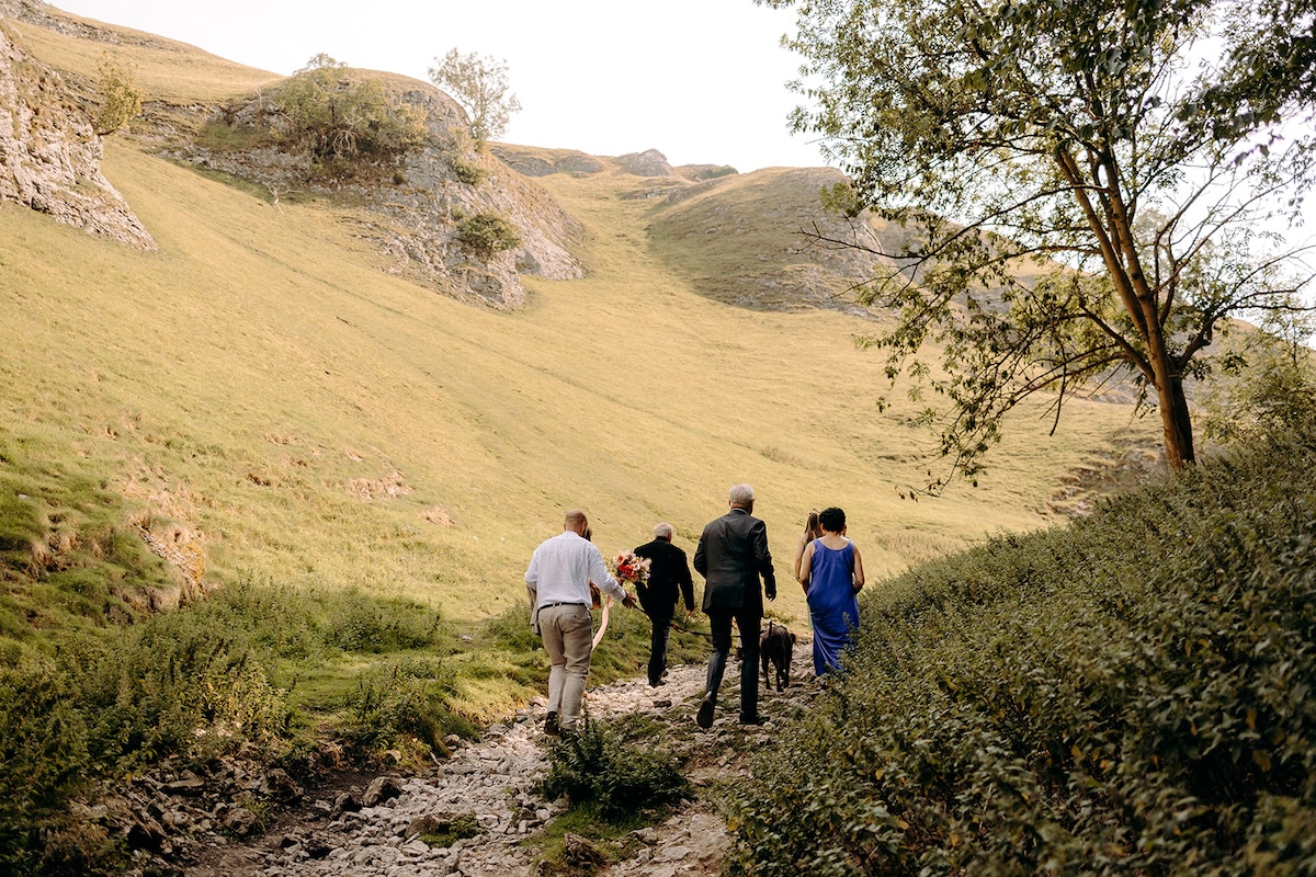 Couple and guests hiking through golden hills toward their secluded Peak District elopement spot.