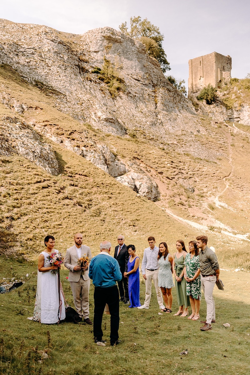 Groom greeting guests beneath rugged cliffs at the start of the outdoor Peak District elopement.