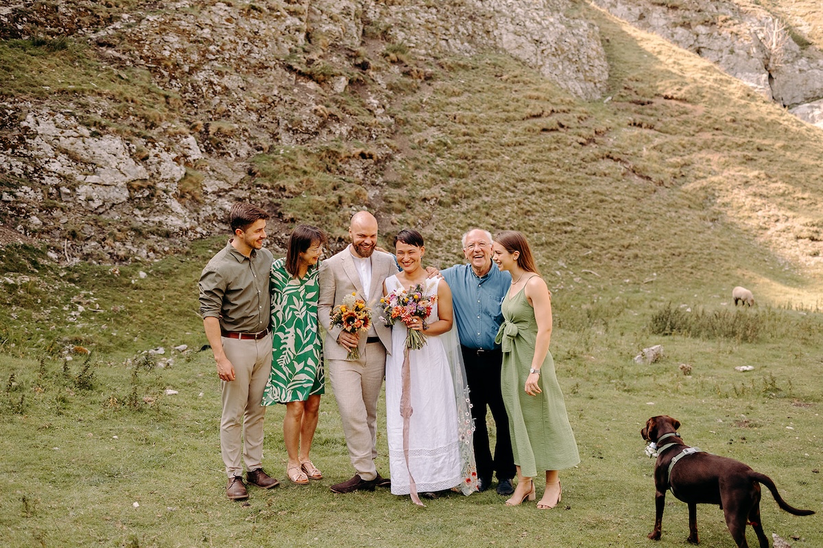 Couple posing with family in the valley while their dog explores nearby.