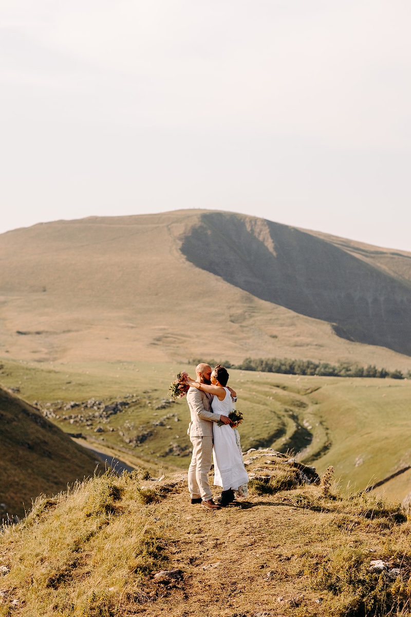 Eloping couple holding hands on a Peak District ridgeline with moorland views behind them.
