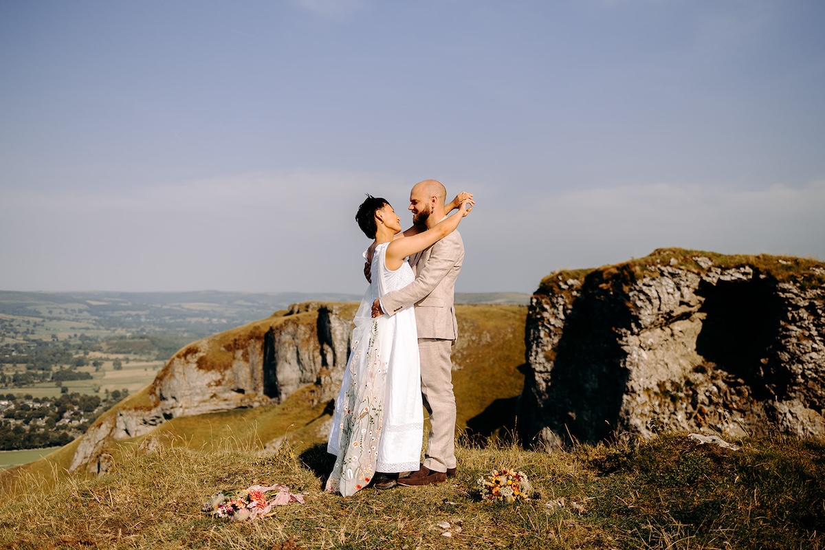 Elopement couple standing on a summit with expansive Peak District countryside behind them.
