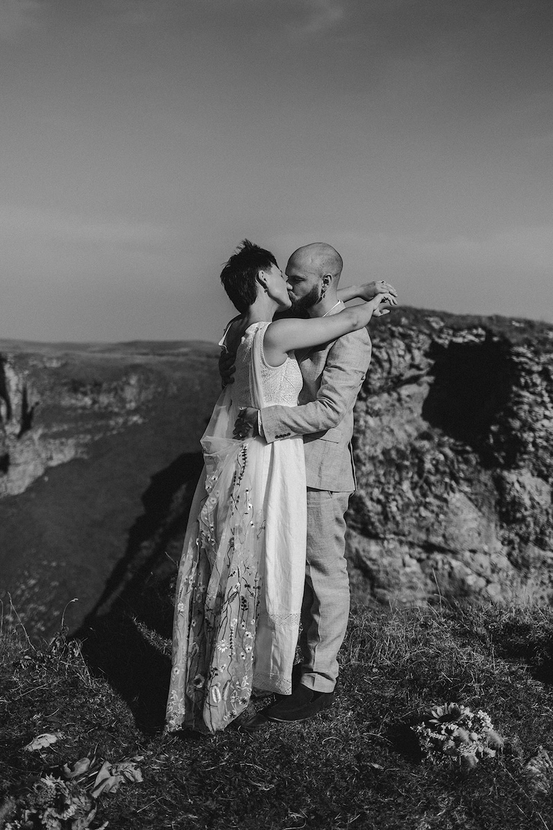 Black and white portrait of a couple holding each other on dramatic Peak District rock formations.
