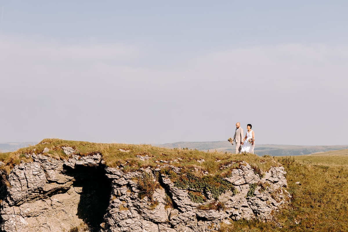 Couple holding bouquet on rugged cliffs documented by a Peak District elopement photographer.