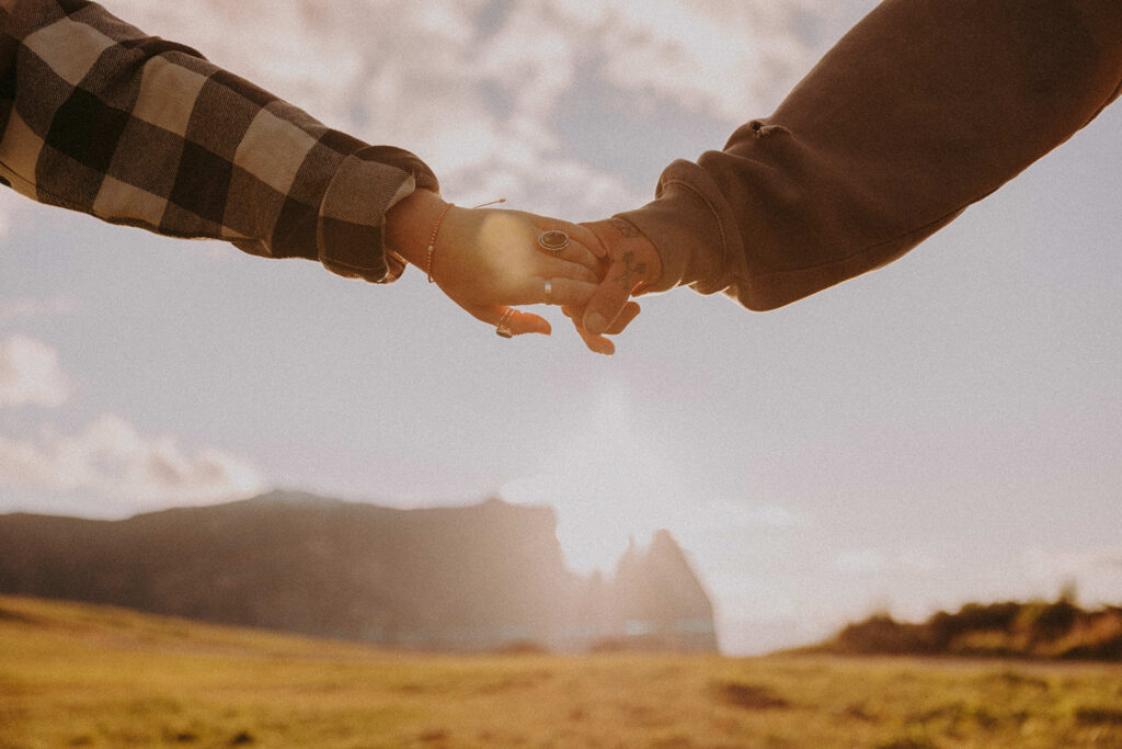 Close-up of couple holding hands during destination pre-wedding shoot in Alpe di Siusi with dramatic mountain backdrop
