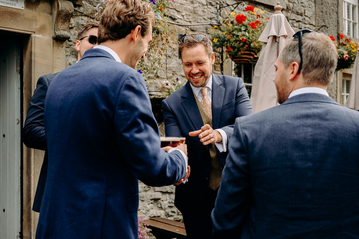 Close candid of groomsmen smiling and talking in the sunshine at Eyam Hall wedding.