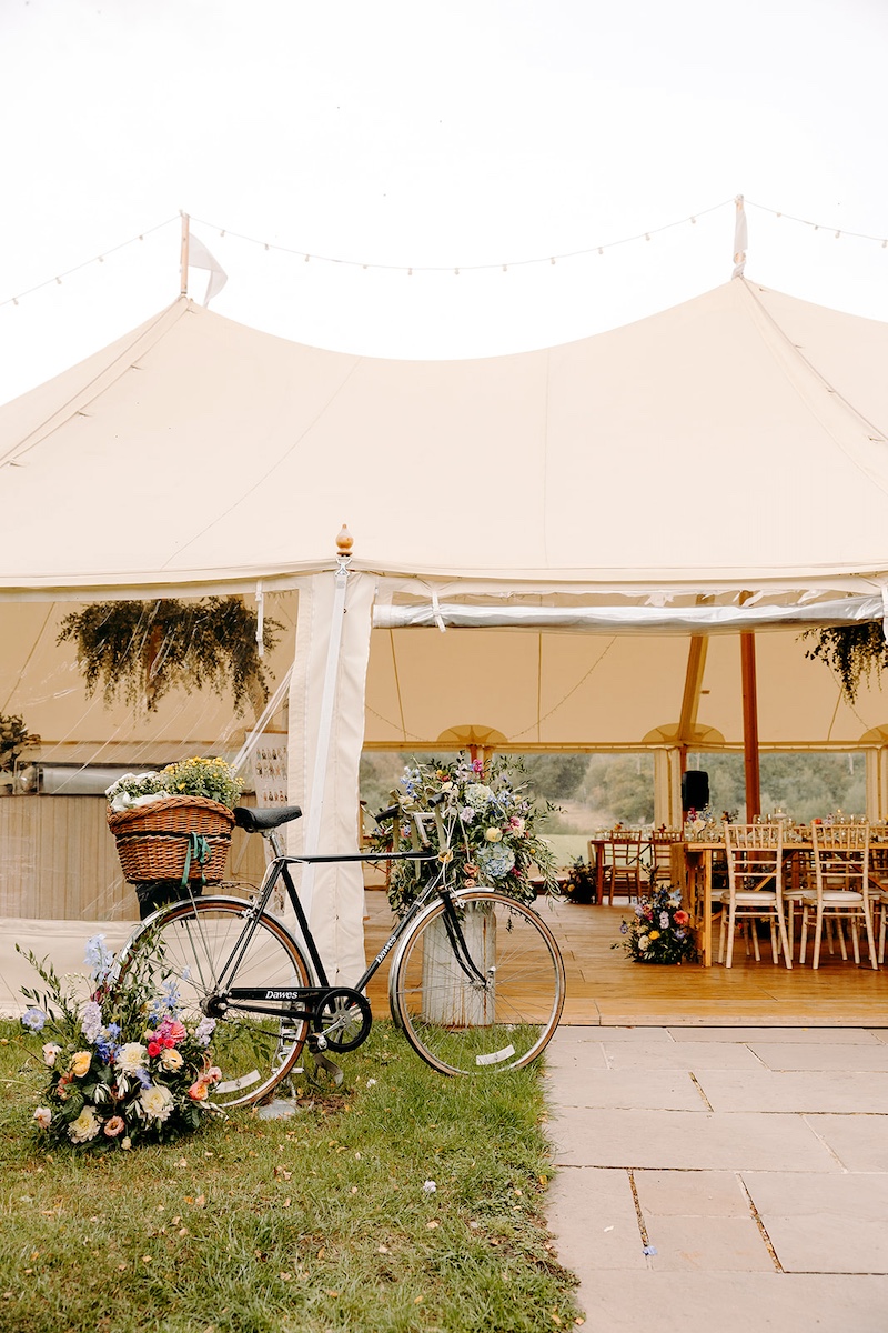 Wide view of beautifully styled marquee with hanging foliage and wooden tables at Eyam Hall wedding.