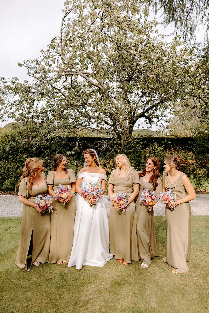 Bridesmaids and bride laughing together holding colourful bouquets at Eyam Hall.