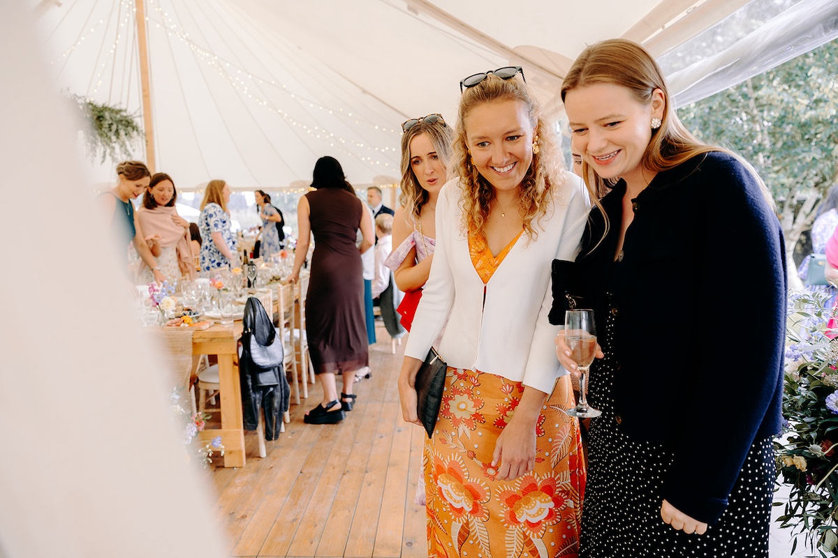 Wedding guests chatting and laughing outside marquee during Eyam Hall reception drinks.