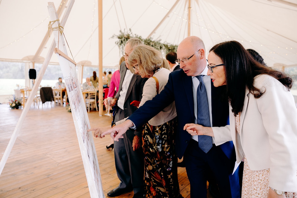 Guests browsing wedding seating plan display and laughing together – Derbyshire wedding photographer candid style.