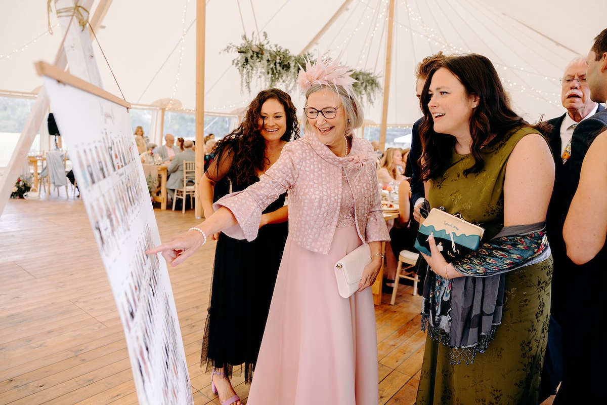 Guests browsing wedding seating plan display and laughing together – Derbyshire wedding photographer candid style.