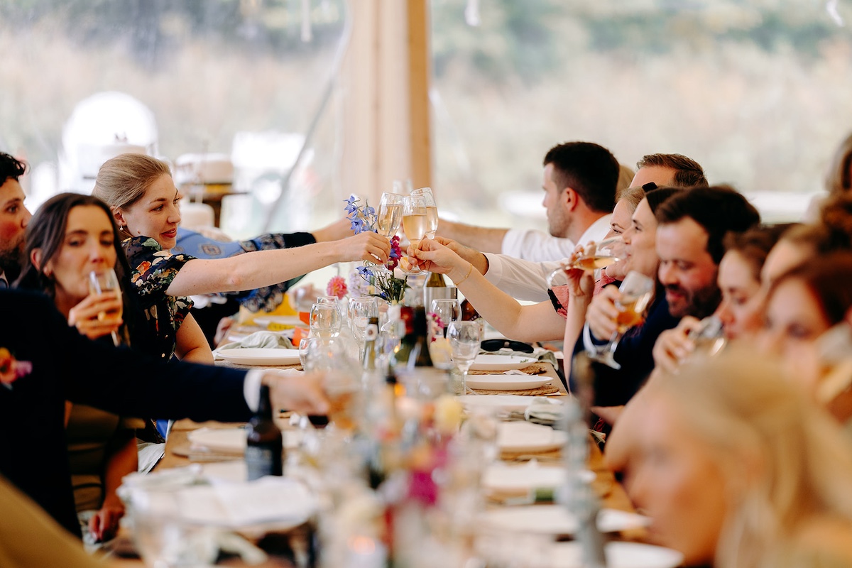 Guests raising glasses and toasting during marquee wedding speeches at Eyam Hall.