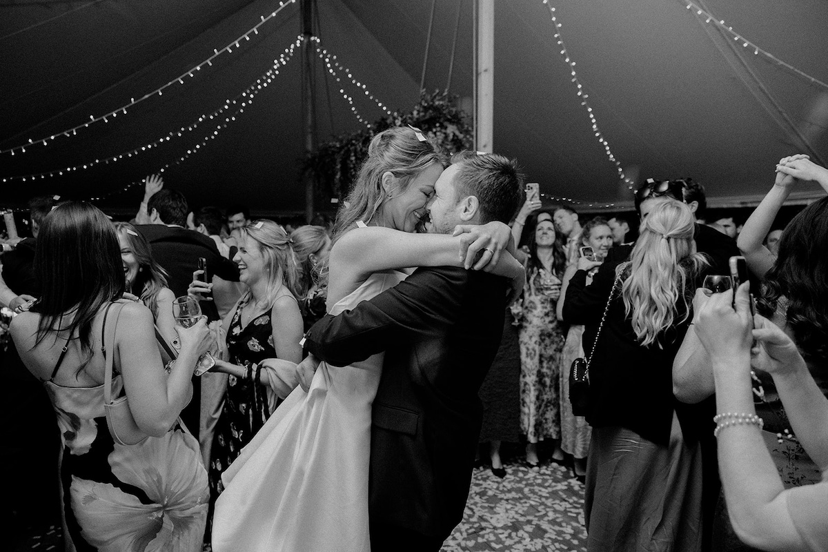 Bride and groom laughing together surrounded by dancing guests at Peak District marquee wedding.